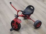 un petit tricycle rouge sur un plancher en bois