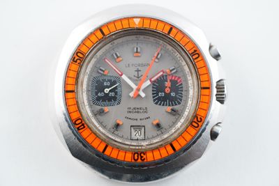 une montre en argent avec un cadran orange sur une surface blanche