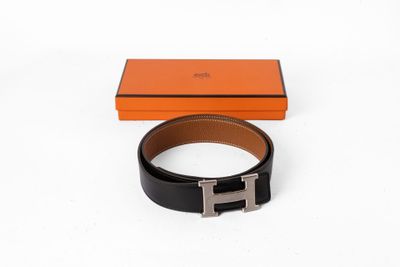 une ceinture noire et orange avec une boucle argentée, posée devant une boîte