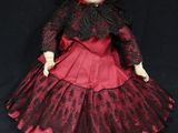 an old fashioned doll with a red dress and black hat