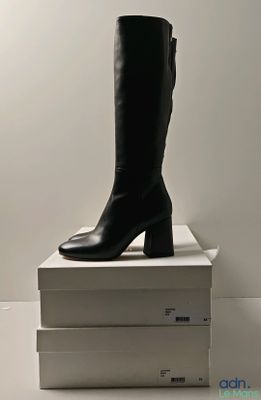 une paire de bottes en cuir noir posée sur une pile de cartons blancs