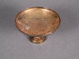 a small metal bowl on a stand on a gray surface