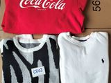 three t - shirts are sitting on a cardboard box with a coca cola logo on it