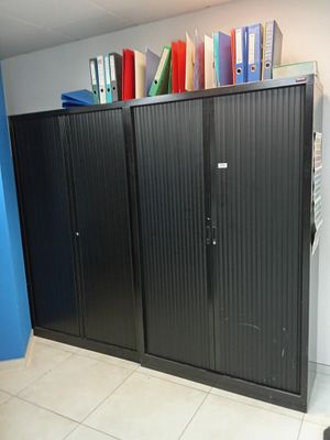 une armoire noire dans un coin d'une pièce, avec des livres posés dessus