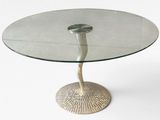 une table en verre avec un piètement en métal, posée sur un sol blanc