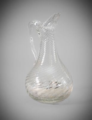 a clear glass vase with a curved handle on a table