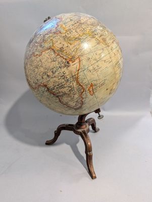 un petit globe terrestre posé sur un trépied, devant un fond blanc