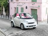 a small white car driving down a cobblestone street
