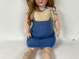 an image of a doll sitting on the ground wearing a blue dress