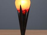 une lampe noire et rouge posée sur une table en bois, près d'un mur gris