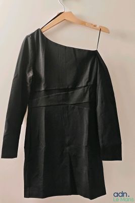 une robe en cuir noir suspendue à un cintre devant un mur blanc
