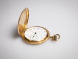une vieille montre de poche avec une chaîne, posée sur une surface blanche
