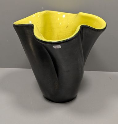 un vase jaune et noir posé sur une table blanche, sur fond gris