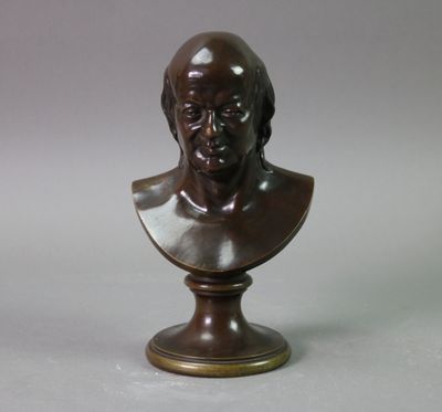 un buste en bronze représentant un homme, posé sur un socle, avec un fond gris