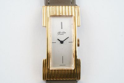 une montre-bracelet en or avec un bracelet marron sur une surface blanche