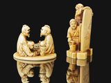 two carved ivory figurines of a man and a woman sitting on a chair