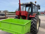 a tractor that is parked next to a green trailer