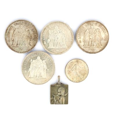 six silver coins and a silver pendant on a white surface