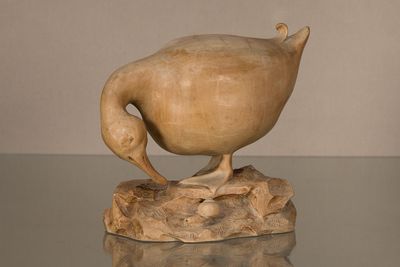sculpture représentant un canard posé sur un rocher, posée sur une table en verre