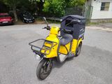 une petite moto jaune garée sur un parking, avec une voiture en arrière-plan
