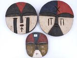 Trois masques africains sont exposés sur un fond blanc