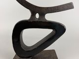sculpture représentant un objet en métal noir incurvé posé sur un socle en bois