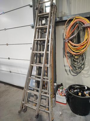une échelle appuyée contre le mur d'un garage, à côté d'une poubelle