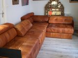 un canapé en cuir marron dans un salon où sont accrochés des tableaux au mur