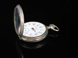 a silver pocket watch sitting on top of a black surface