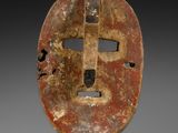 un masque en bois posé sur un socle, sur une surface blanche