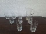 six verres et un pichet posés sur une table en bois