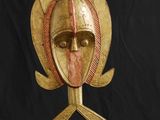 un gros plan d'un masque en bois posé sur un socle, sur fond noir