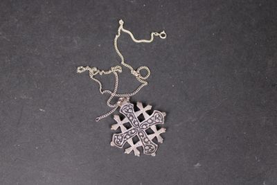 pendentif en forme de croix en argent avec une chaîne, sur un fond noir