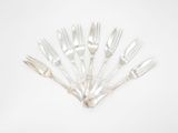 six fourchettes en argent disposées en cercle sur une surface blanche