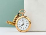 a gold pocket watch sitting on a table next to a wall