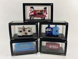 quatre petites voitures emballées dans leur boîte, exposées dans une vitrine posée sur une surface blanche