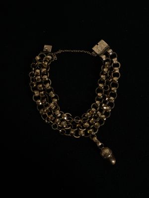 un collier composé d'une chaîne à laquelle est suspendue une clochette