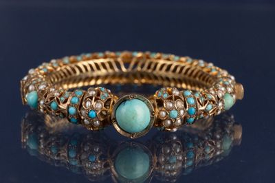 un gros plan d'un bracelet en or et turquoise posé sur une surface noire
