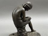 bronze statue of a man sitting on a rock with his hands on his knees