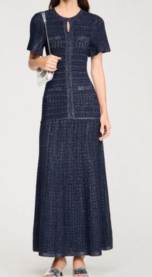 La femme porte une robe bleue et des sandales, et tient un sac à main.