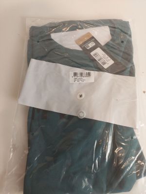 deux paires de pantalons verts pour homme, dans des sacs en plastique, posées sur une table