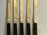 four knives are lined up on a table with a white cloth
