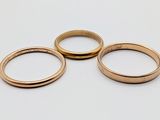 three gold wedding rings sitting on top of each other on a white surface