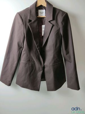 un blazer marron suspendu à un cintre sur un mur blanc