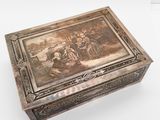 une vieille boîte en argent ornée d'une peinture, posée sur une surface blanche