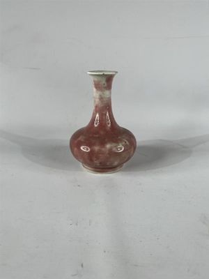 un petit vase rouge posé sur une surface blanche