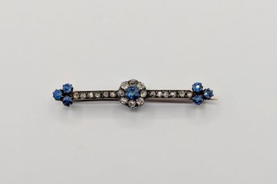 un gros plan sur une broche en forme de barre, ornée de diamants bleus et blancs