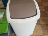 a white toilet and a green trash can on the floor