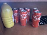 several cans of coca cola are lined up next to a bottle of orange juice
