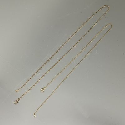 trois colliers en or posés sur une surface blanche